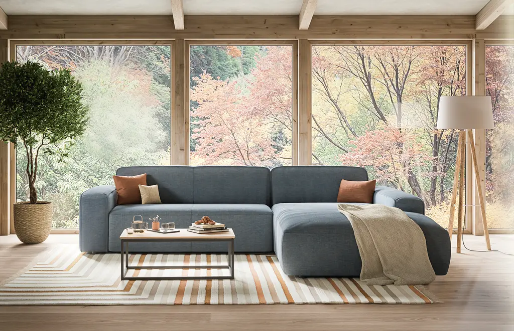 Offener natürlicher Raum mit blauem Sofa in der Mitte und großem Fenster mit Naturblick dahinter.